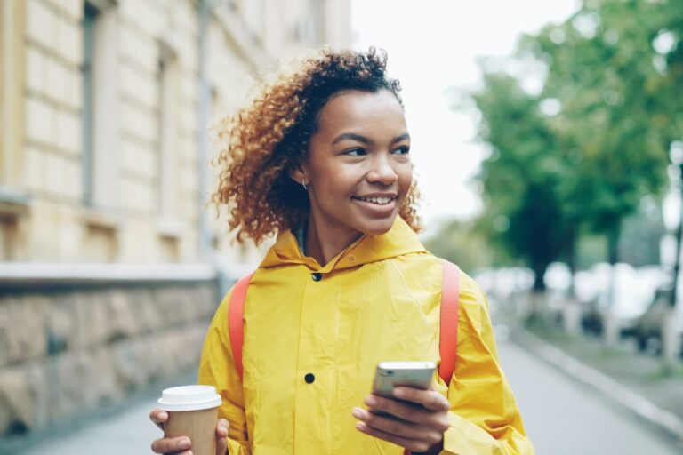 woman-in-yellow-raincoat-holding-coffee-and-phone