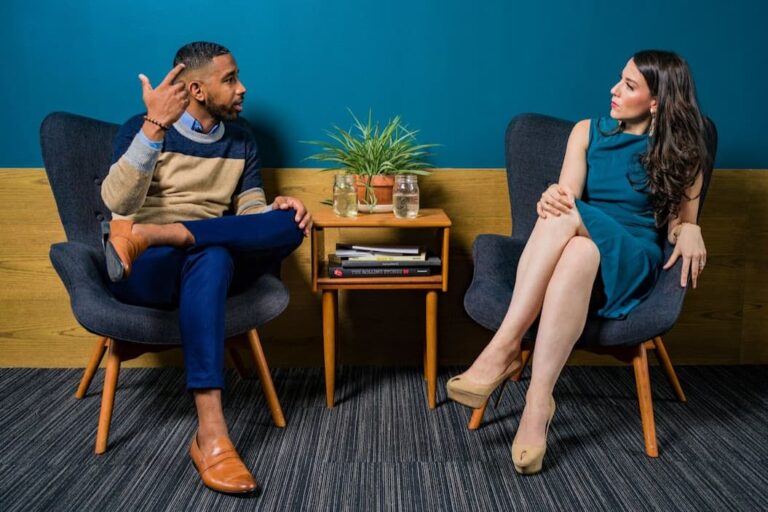 woman-wearing-teal-dress-sitting-on-chair-talking-to-man