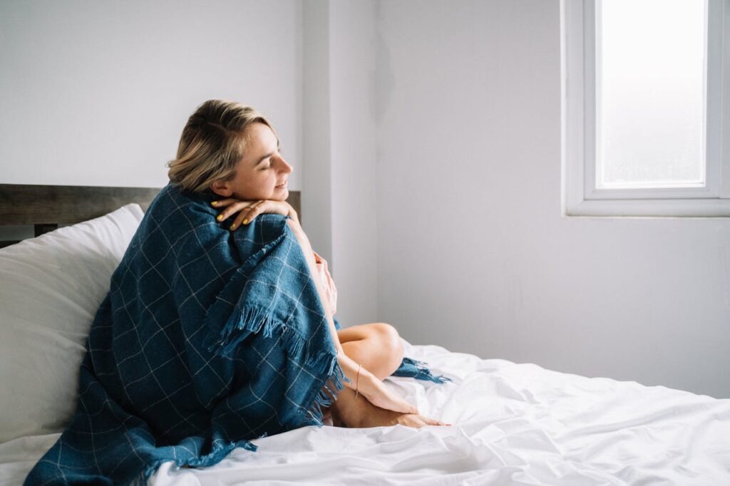 woman-covered-with-a-blue-blanket-sitting-on-bed