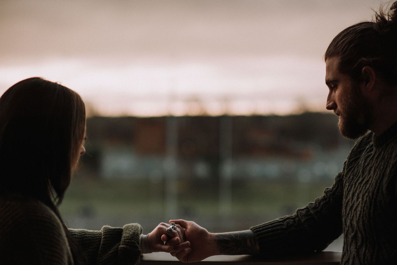 crop-couple-holding-hands-on-balcony-at-sunset