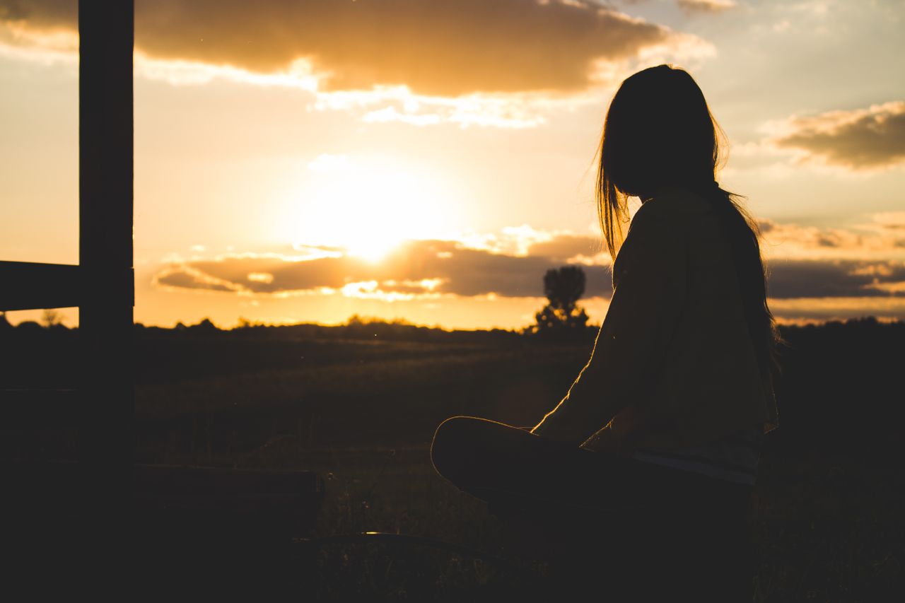 silhouette-photo-of-woman-sitting-near-trees-during-golden-hour