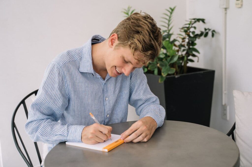 a-smiling-young-man-sitting-at-a-table-taking-notes