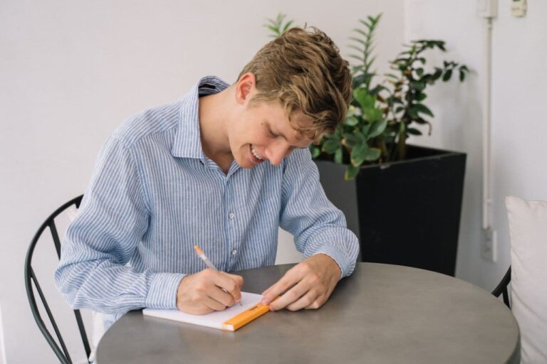 a-smiling-young-man-sitting-at-a-table-taking-notes